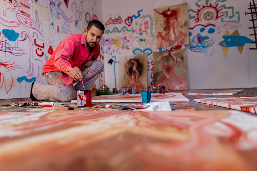 Skilled man, an artist, from his home art studio, painting the canvas, with oil paints, motivated by red color