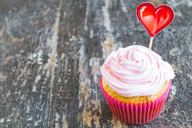 istock Coconut cupcake with pink curd cream on wooden background 1424980838