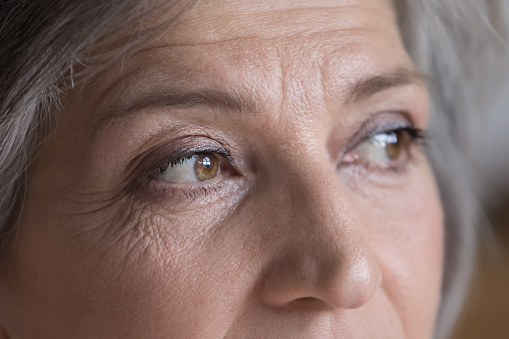 Upper face of serious senior woman looking away. Brown eyes with makeup, mascara, facial skin with wrinkles close up. Female portrait cropped shot. Elderly age, eyesight, beauty, healthcare