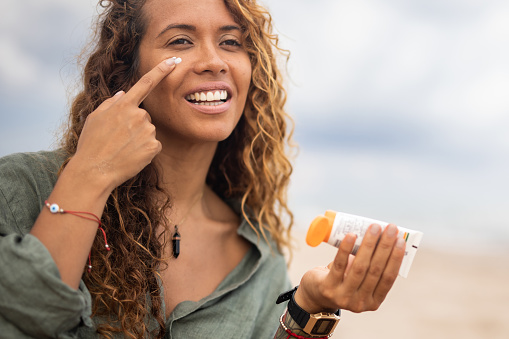 A beautiful cheerful Spanish woman applies sunscreen to her face, enjoying her vacation and a little luxury in her life.