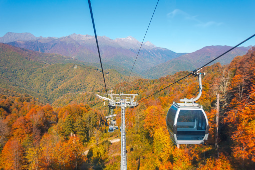 Cabins on lifts go up to the mountains around the landscape of the autumn season with bright yellow foliage on the slopes of the mountains