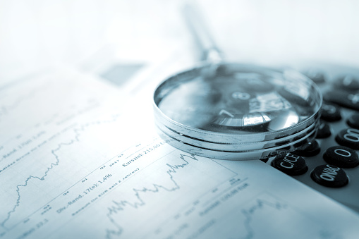 Magnifying glass, calculator and charts on paper symbolizing business and financial market. Blue toned image. studio shot in raw format taken with prime lens for best quality