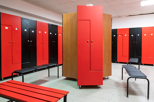 Empty changing room in fitness gym with group of red and black wooden lockers standing in a row by wall. Selective focus. Healthy lifestyle theme.