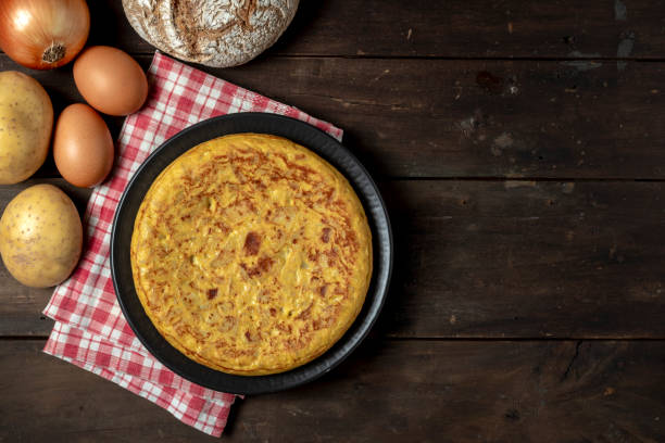 POTATOES OMELETTE AND SEVERAL INGREDIENTS ON DARK WOODEN TABLE. TYPICAL SPANISH FOOD CONCEPT. COPY SPACE. TOP VIEW. POTATOES OMELETTE AND SEVERAL INGREDIENTS ON DARK WOODEN TABLE. TYPICAL SPANISH FOOD CONCEPT. COPY SPACE. TOP VIEW. omelet rustic food food and drink stock pictures, royalty-free photos & images