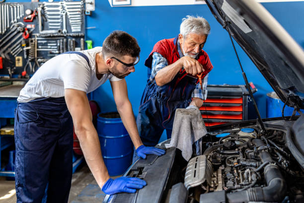 a senior mechanic man and a male colleague are checking the oil in a car. - old men car oil imagens e fotografias de stock