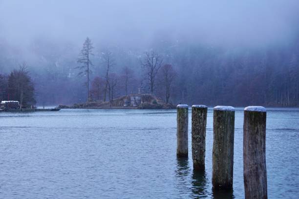 туманное утро на озере кёнигзее в баварии. остров в тумане, памятник на острове в тумане. голубой лес и туман на озере. - konigsee стоковые фото и изображения