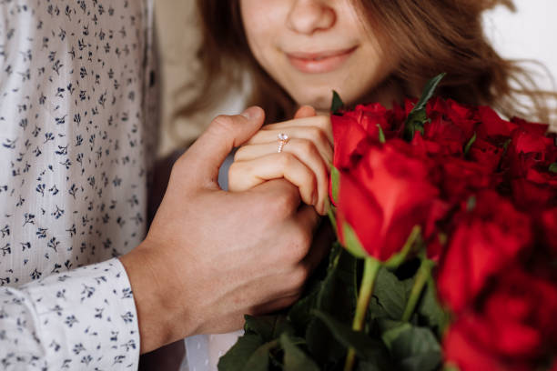 istock young man holding his fiance's hand with gold ring while making a marriage proposal with bouquet of red roses. Engagement of a young couple in love. The concept of love and togetherness. 1425017741
