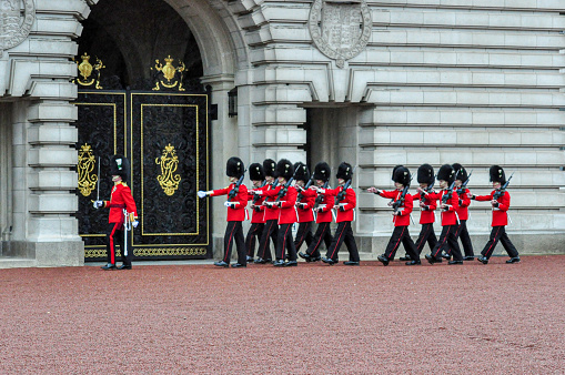 Armed soldiers using bearskin are forming in the front yard at Buckingham Palace, London, England. This picture was taken from outside the palace during the changing ot The Queen's Guard, the infantry soldiers charged with guarding the official royal residences in the United Kingdom. A bearskin is a tall fur cap, usually worn as part of a ceremonial military uniform.
