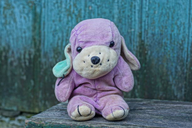 one small plush purple white toy dog stands on a gray wooden table against a green wall