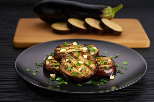 Salad with grilled eggplant, parsley and garlic on a black plate,selective focus.whole eggplant background. stock photo