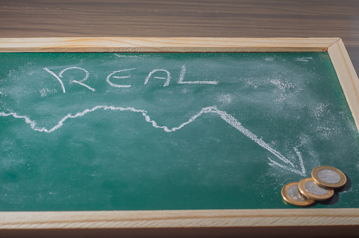Green chalkboard With the word Real written with white chalk and a graphics with a plummeting arrow,copy space.