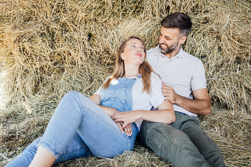 Portrait of couple sitting on the hay and enjoying on the ranch.