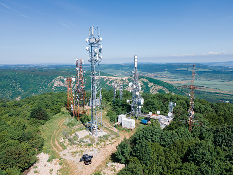 Drone view of group of telecommunications towers surrounded by green forest trees. Technology and Global Business.