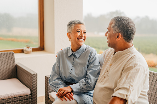 Love, happy and laugh with senior couple sitting together at home and enjoying retirement and free time together. Smiling man and woman bonding and showing affection while sharing a romantic moment