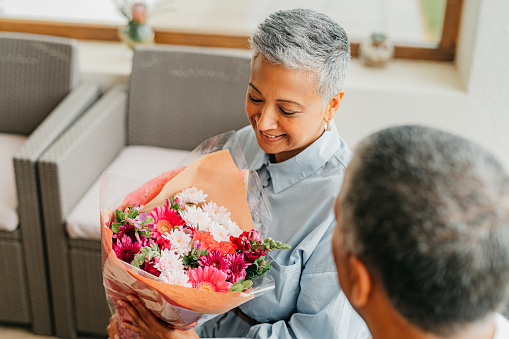Man surprise woman with flower bouquet for love, senior couple in celebration of marriage and wedding anniversary in house. Happy, smile and elderly people with gift to celebrate retirement in home