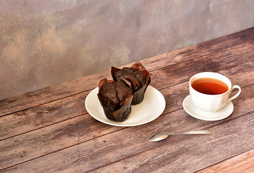 A plate with two chocolate muffins and a cup of hot tea on a wooden table. Close-up.