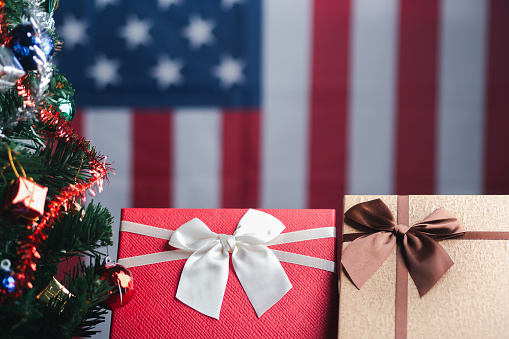 Close-up of gift boxes and a Christmas tree with an American flag in the background. Space for text. Concept of Christmas and new year festival.