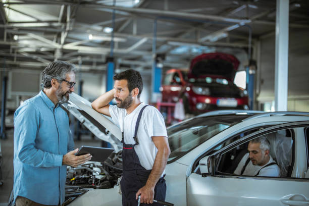 Manager and auto mechanic working on digital tablet in a repair shop. Mid adult inspector and auto repairman talking while using touchpad in a workshop. auto repair shop mechanic digital tablet customer stock pictures, royalty-free photos & images