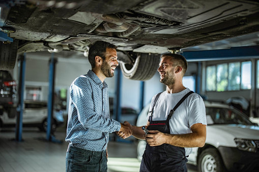 Satisfied customer shaking hands with auto mechanic in repair shop.