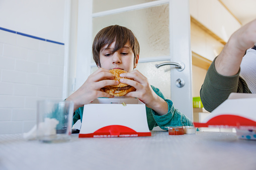 Boy sitting at the dining room table, eating junk food burger directly from box