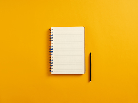 Blank or empty notepad and black pen on yellow background with copy space.