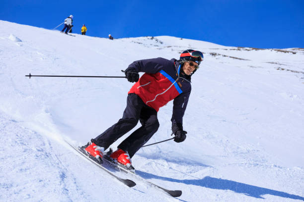 Vital senior,  men snow skier skiing, enjoying on sunny ski resorts. Skiing carving at high speed against blue sky. stock photo