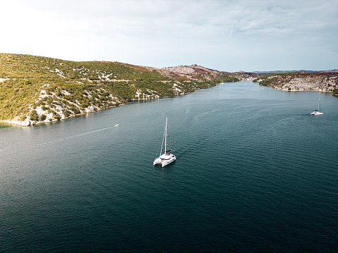 View from above, stunning aerial view of a catamaran sailing by the coast of Croatia in the Adriatic sea. No wind, engine power only.