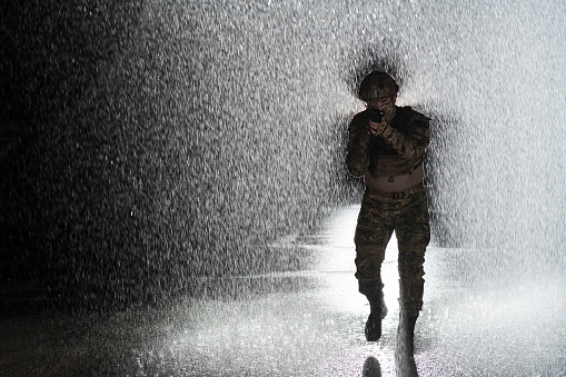 Army soldier in Combat Uniforms with an assault rifle, plate carrier and combat helmet going on a dangerous mission on a rainy night. High quality photo