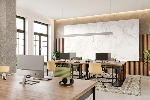 Modern open plan office interior. Large desk, chairs, computers, headphones, pendant lamp, carpet on concrete floor, marble panel and decoration. Template for copy space. Render.