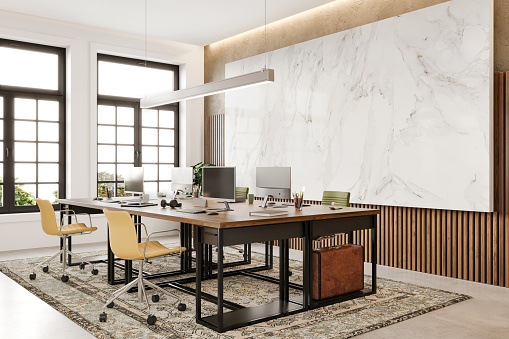 Modern open plan office interior. Large desk, chairs, computers, pendant lamp, carpet on concrete floor, marble panel and decoration. Template for copy space. Render.