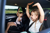Two caucasian female children riding in the car in the back seat and dancing
