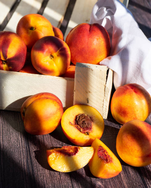 eine schachtel mit leckeren frischen pfirsichen auf dem tisch. pfirsiche in einer alten rustikalen box auf einem dunklen holztisch. - nectarine stock-fotos und bilder