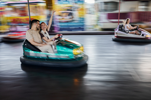 Happy couple having fun while driving bumper car at amusement park. Blurred motion. Copy space.