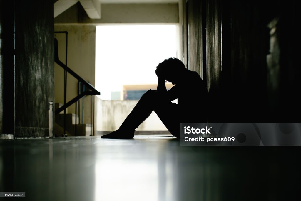 Silhouette of depressed man sitting head in hands on the walkway of residence building. Sad man, lonely and unhappy.Negative emotion and mental health concept. The impact of Economy crisis. dramatic. Bullying Stock Photo