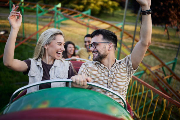 istock Happy couple riding on rollercoaster with raised arms at amusement park. 1425113023