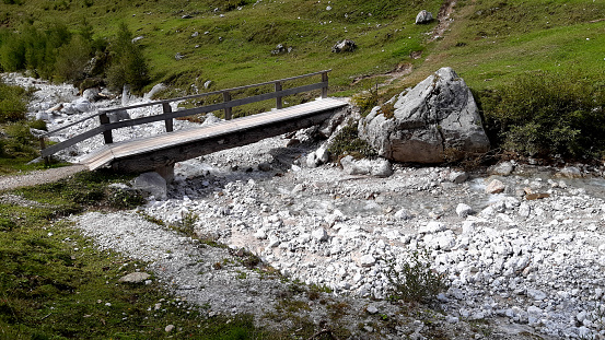 crossing a watercourse high in the mountains. limestone boulders and clear cold glacial water over which a tree trunk bridge and wooden railing is built. uncertainty over flooded water