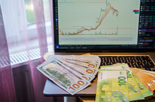 Stack of US Dollar and Euro banknotes on computer screen and monitor with stock chart