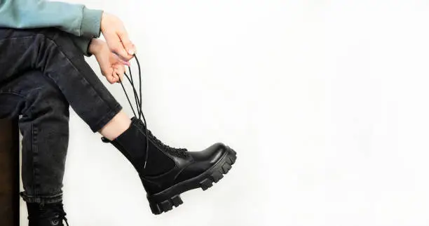 Fashionable, black leather lace-up boots. Youthful, stylish collection of women's shoes. The girl puts on shoes. Close-up. White background.