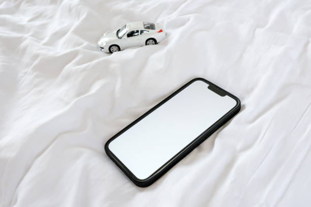 Smartphone and die cast model car on bed. Mobile phone device with blank white mockup screen as copy space.