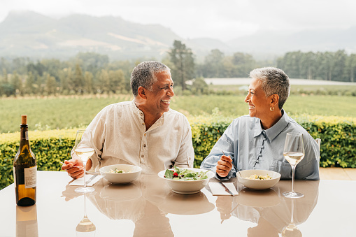 Senior couple eating food on vineyard, lunch at wine farm during holiday in Italy for retirement and luxury vacation in the country side. Happy, smile and love elderly man and woman in nature