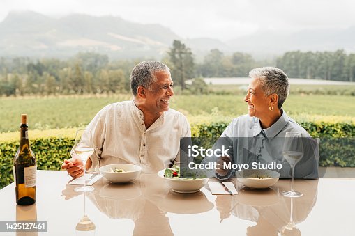 istock Senior couple eating food on vineyard, lunch at wine farm during holiday in Italy for retirement and luxury vacation in the country side. Happy, smile and love elderly man and woman in nature 1425127461