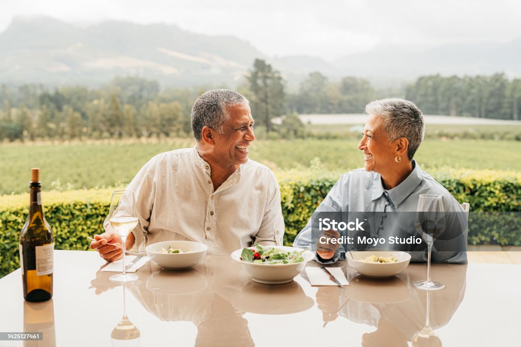 Senior couple eating food on vineyard, lunch at wine farm during holiday in Italy for retirement and luxury vacation in the country side. Happy, smile and love elderly man and woman in nature Couple - Relationship Stock Photo