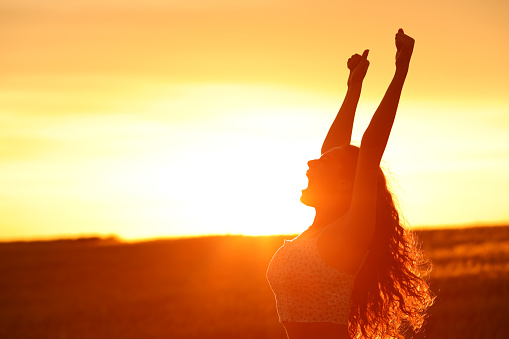 Excited woman raising arms at sunset celebrating