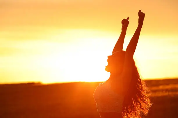 Photo of Excited woman raising arms at sunset celebrating