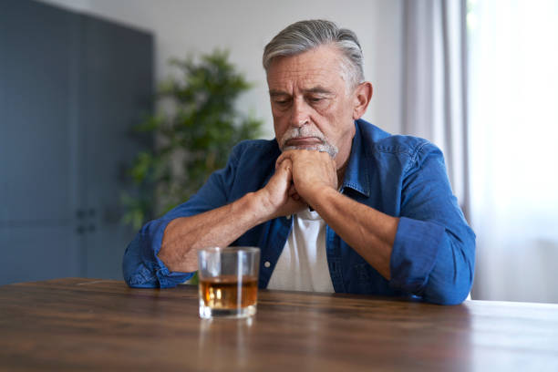 Senior caucasian man sitting and looking at the glass with whiskey at home stock photo