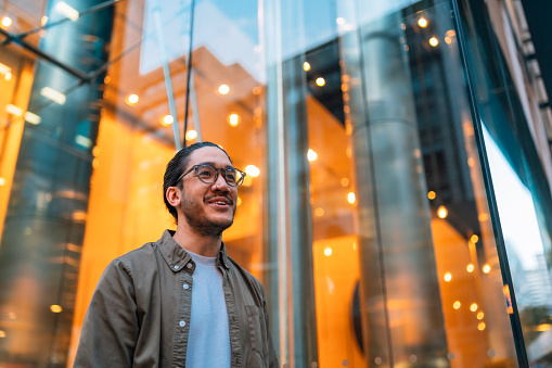 Happy man outside an office building looking up and wearing eyeglasses.