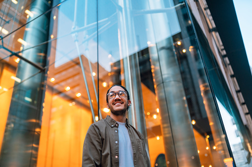 Happy man outside an office building looking up and wearing eyeglasses.