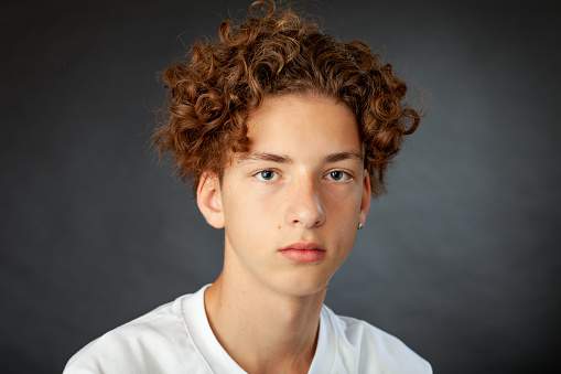 Close-up studio portrait of a 15 year old teenager boy with an earring in a white t-shirt on a black background