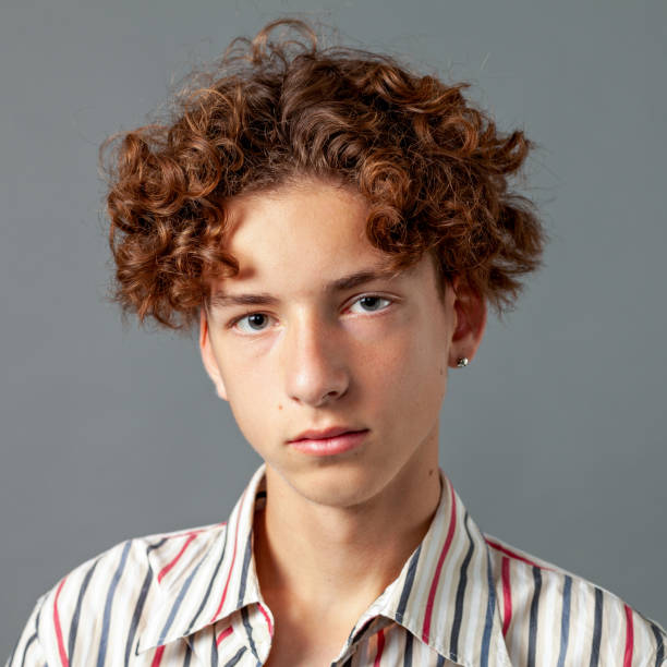 Close-up studio portrait of a 15 year old teenager boy with an earring in a striped shirt on a gray background stock photo