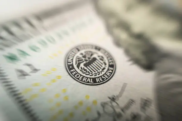 Photo of Selective focus on US Federal Reserve emblem on hundred dollars banknote as FED consider interest rate hike, economics and inflation control national organization.